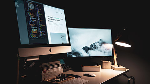 A dual monitor setup on a desk, in a dimly-lit office