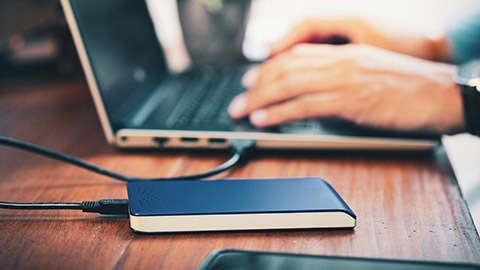 A designer working on a laptop with an external HD alongside