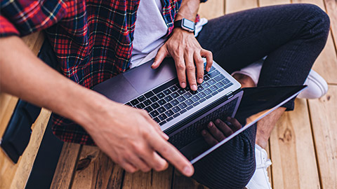 An IT professional sitting outside, with their legs crossed nursing their laptop