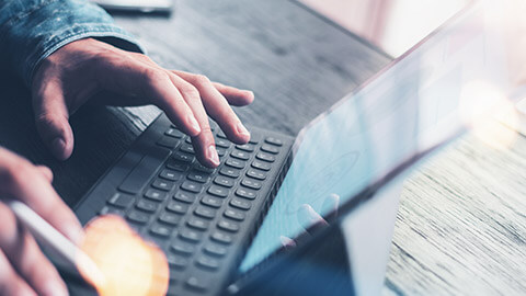 A close view of a person typing on a wireless keyboard and tablet