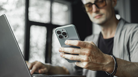 Man using computer while looking at the phone