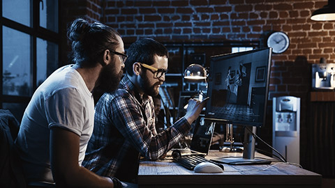 Side view of diverse group of men sitting at table with computer and coworking on creation of new cartoon movie