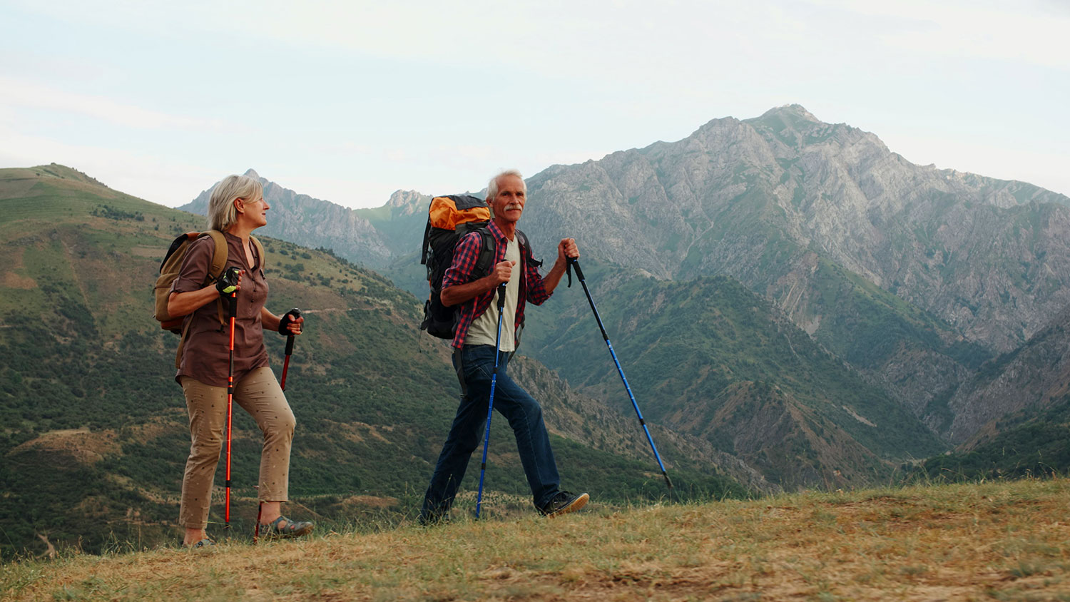 Active senior caucasian couple hiking in mountains with backpacks, enjoying their adventure 4k