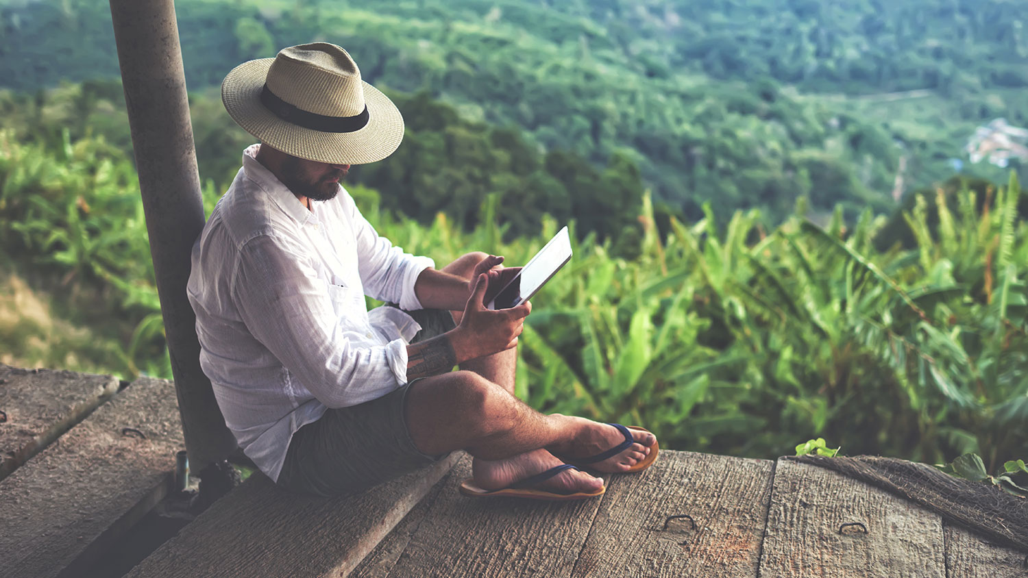 Male tourist is holding touch pad, while relaxing outdoors during his trip in Thailand