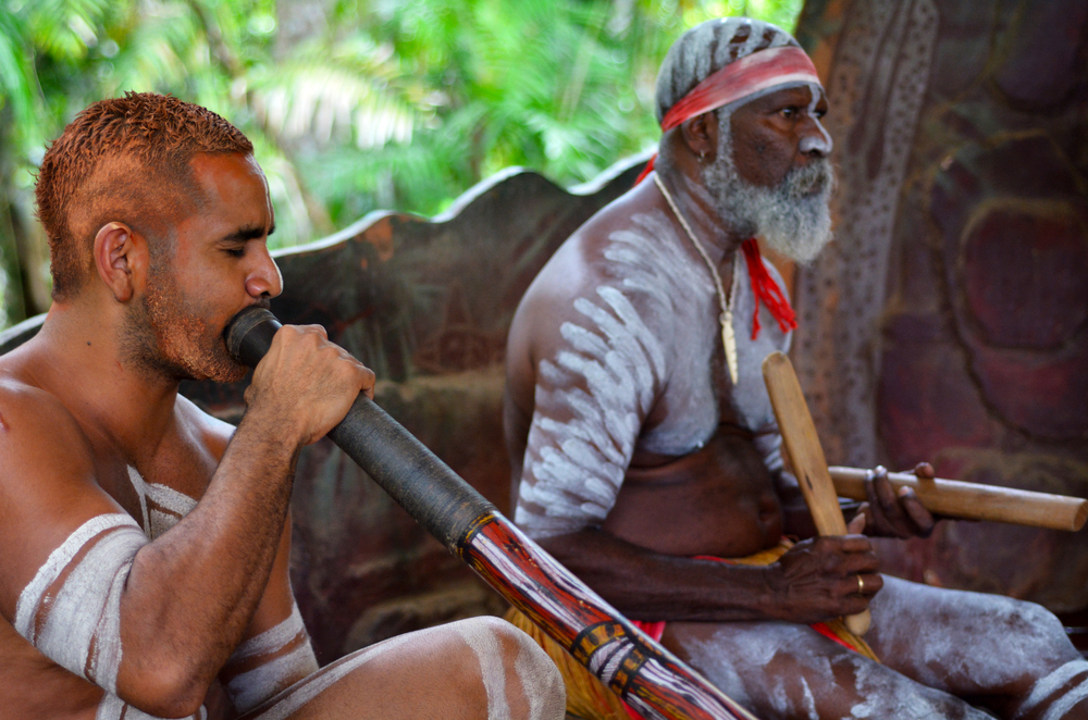 Australian Aboriginal men play Aboriginal music on didgeridoo and wooden instrument during Aboriginal culture show in Queensland, Australia.