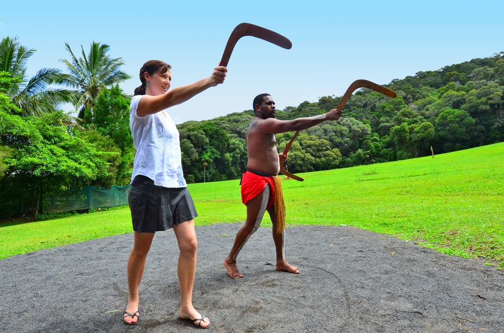 Indigenous Australian man teaches a young Australian woman how to throw a boomerang during cultural show in Queensland