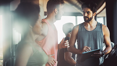 Male trainer talking to male client while holding clipboard