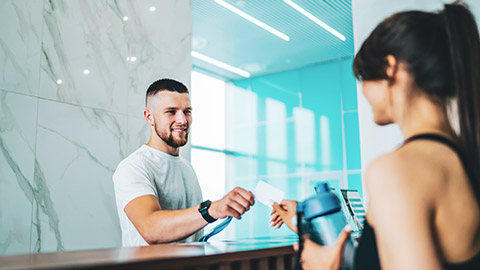 Male trainer handing card to female client in gym