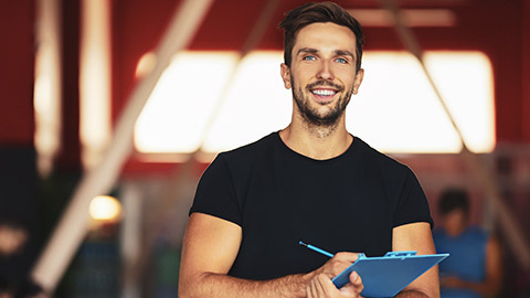 Young male trainer smiling and holding clipboard with training documents on it