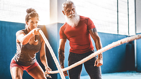 Hipster trainer supervising female client doing battle rope exercise