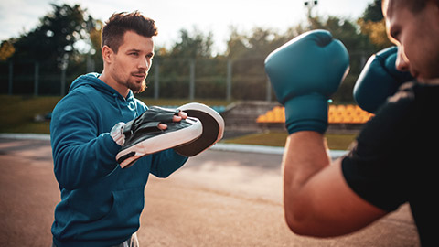 Male trainer doing boxing exercises with client outdoors