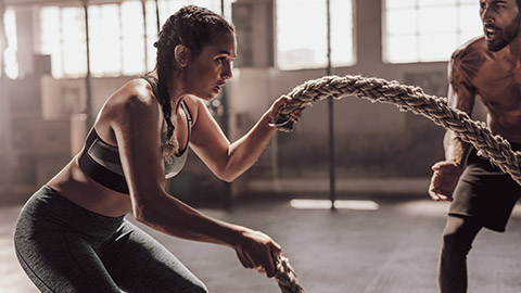 woman using battle rope with trainer in background