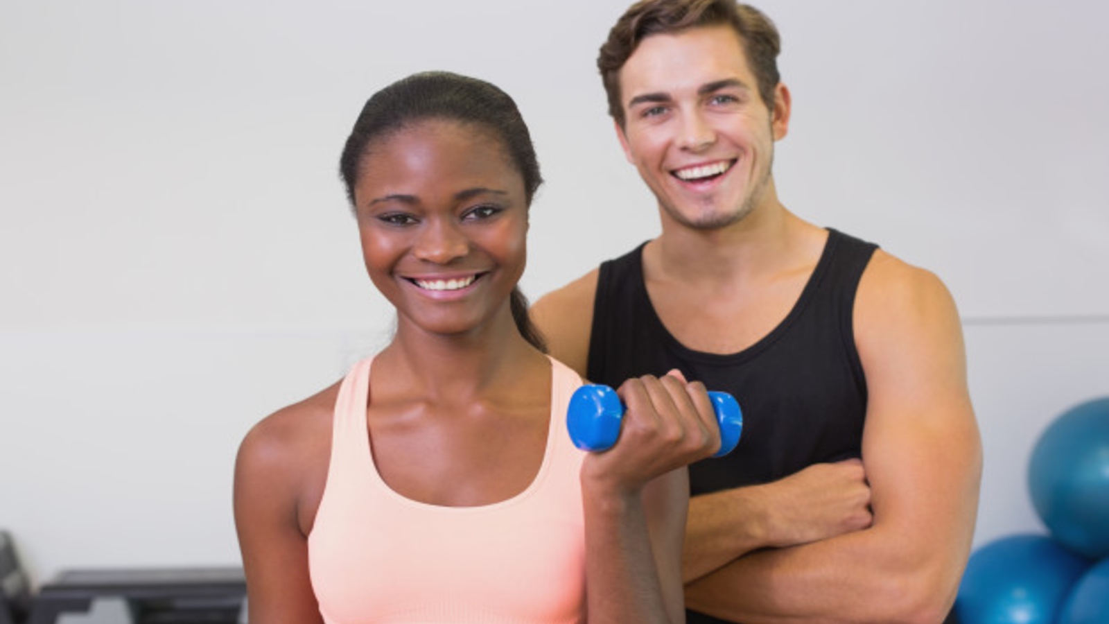 Male fitness professional monitoring a female client who is using free weights