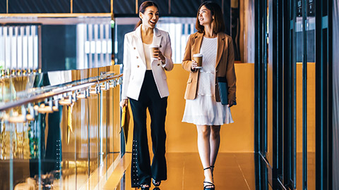 2 young asian female professionals walking and talking in a modern office environment