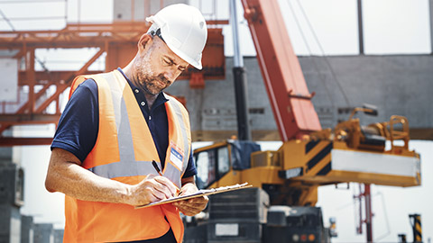 Worker on construction site wearing safety gear and writing on a clipboard