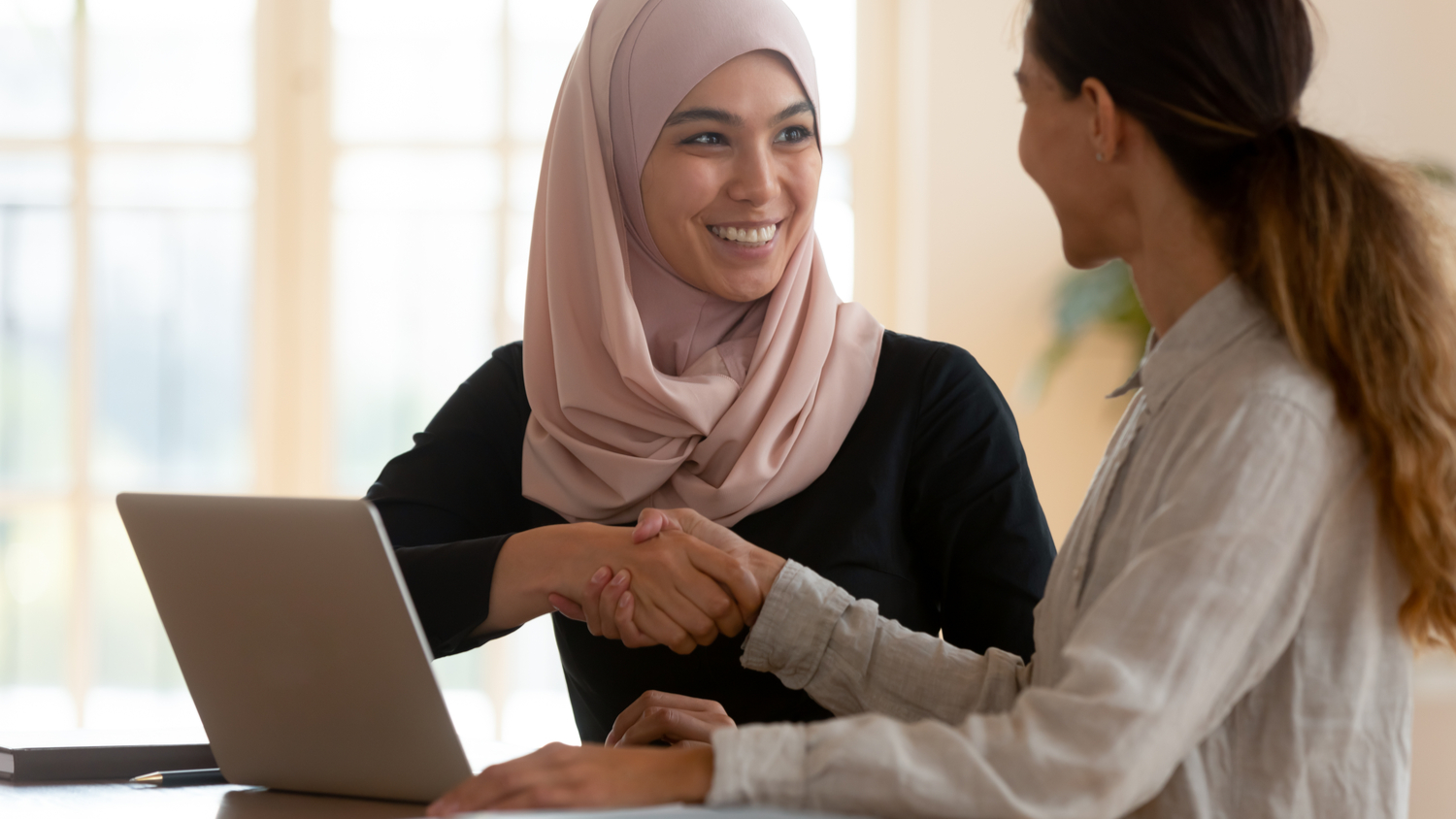 Happy female asain muslim business leader shake hand of caucasian employee