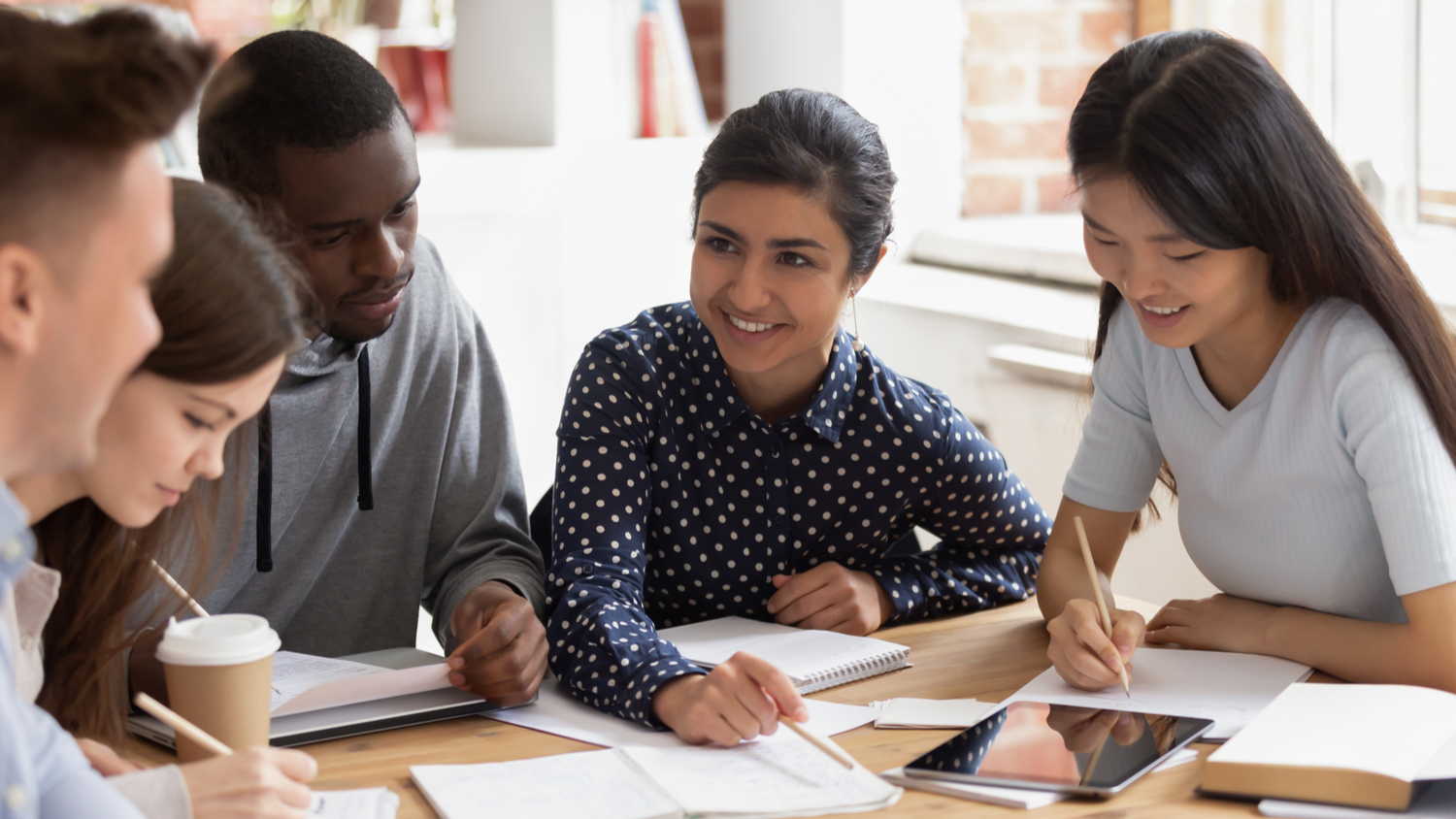 Focused multi national students studying together, team of girls and guys led by indian leader help with home work understanding, share ideas, offers creative approach to solve math challenge concept