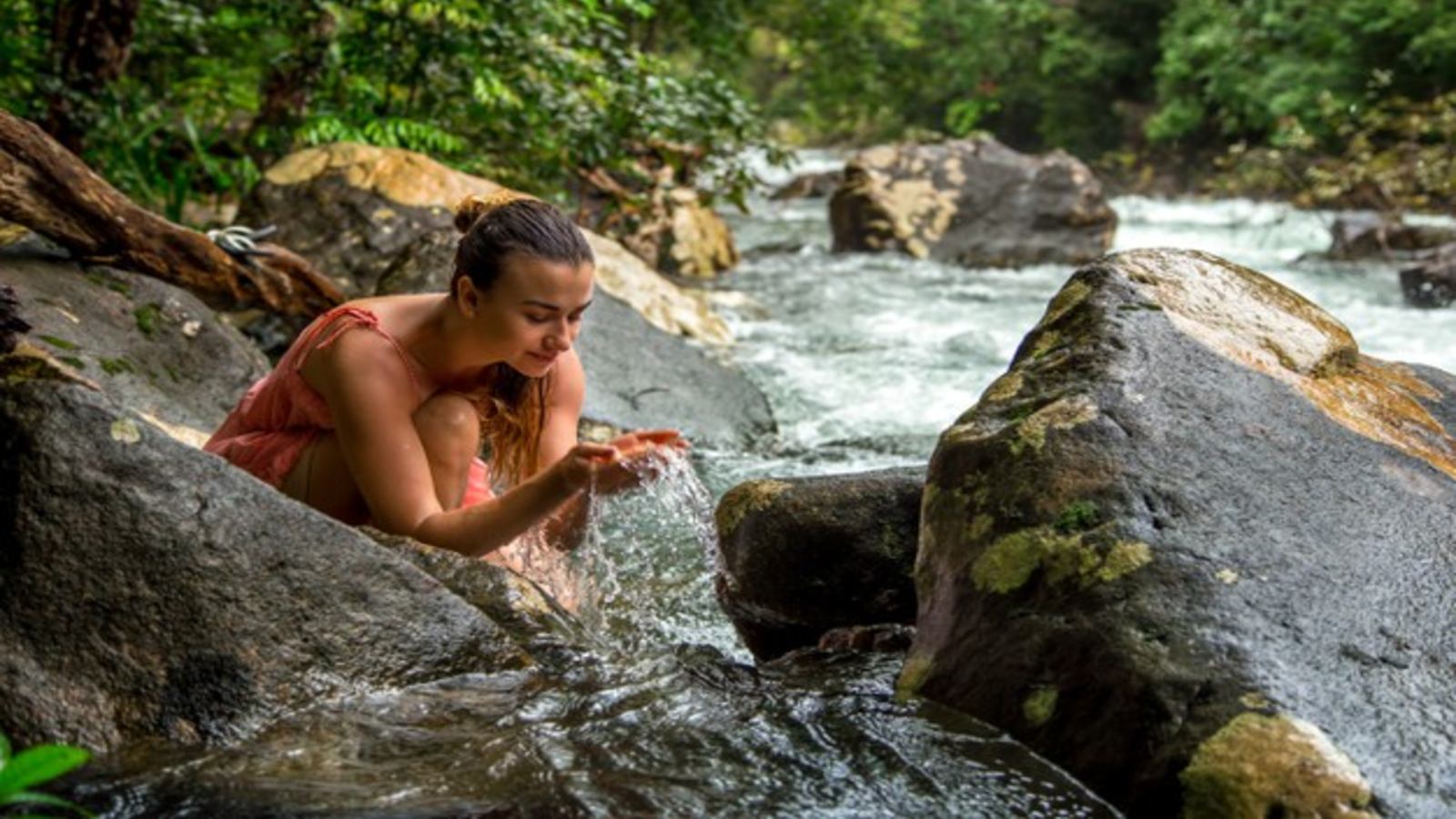 young girl drinks water from a stream