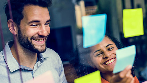 Smiling coworkers with sticky notes on a window