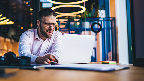 Male sitting at desk in modern office talking to colleague on laptop