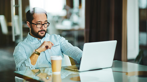 Asian male sitting at desk in office with laptop