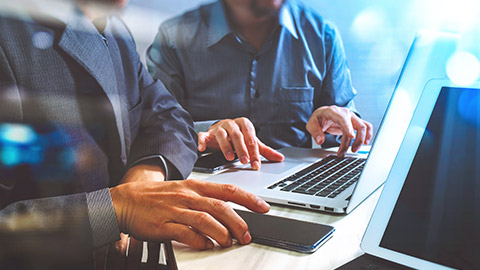 Two accountants sitting at a desk looking at accounting software on a laptop