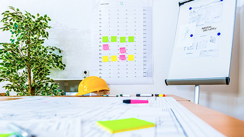 Low view of table with construction plan, scheduling board, sticky notes and hard hat