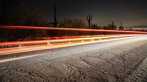 A time-lapse of a car driving down a desert highway at night